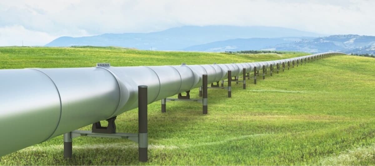 Tubería especial de gran diámetro atravesando un paisaje verde, sostenida por soportes, con un fondo montañoso y cielo nublado.