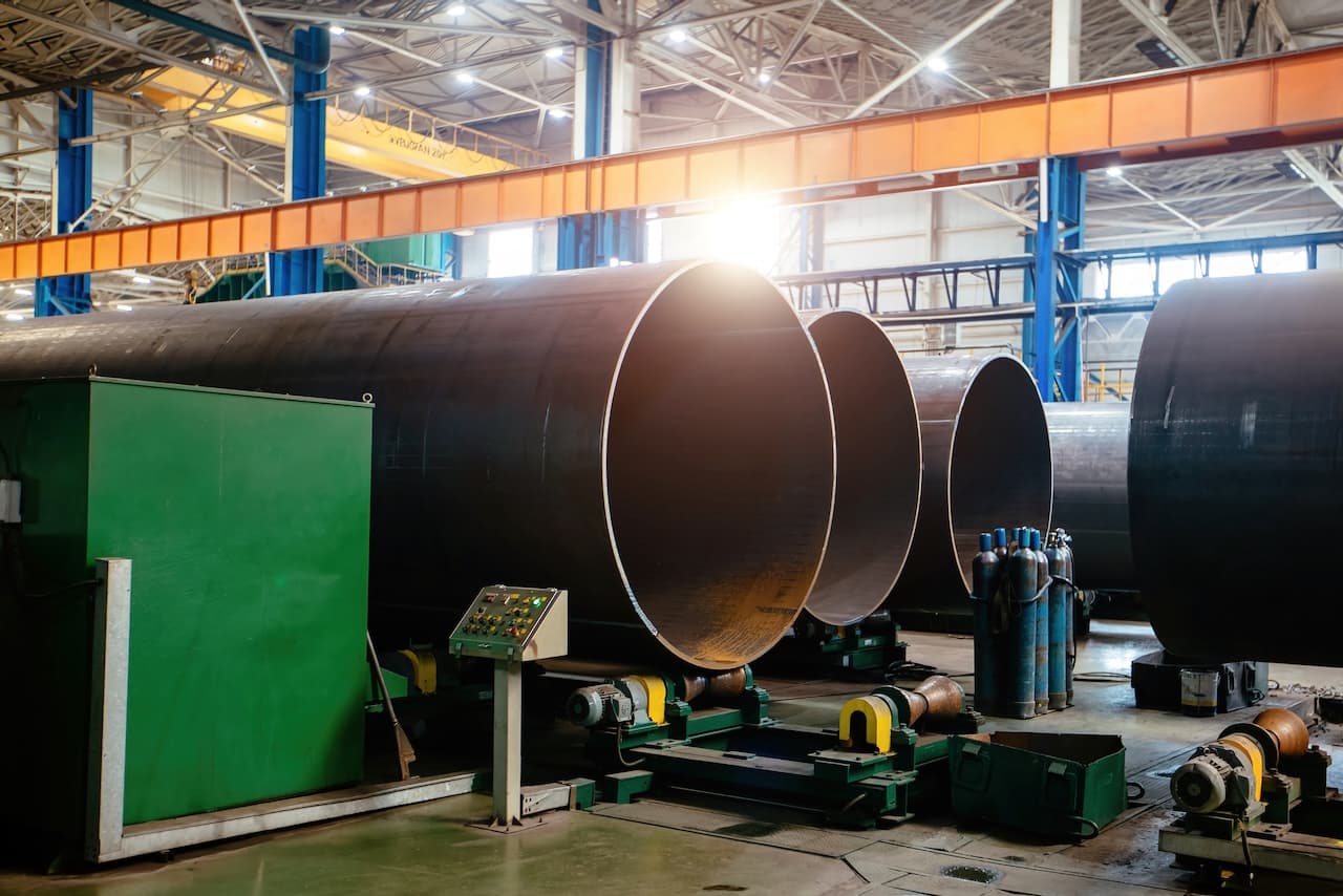 Tubería de Diámetros Mayores en una fábrica, con un área de trabajo iluminada, maquinaria y equipo para el manejo de tubería.
