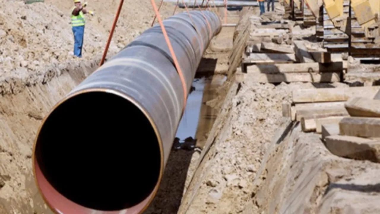 Tubería de Diámetros Mayores siendo instalada en una zanja, con trabajadores supervisando la operación y el terreno alrededor lleno de tierra.